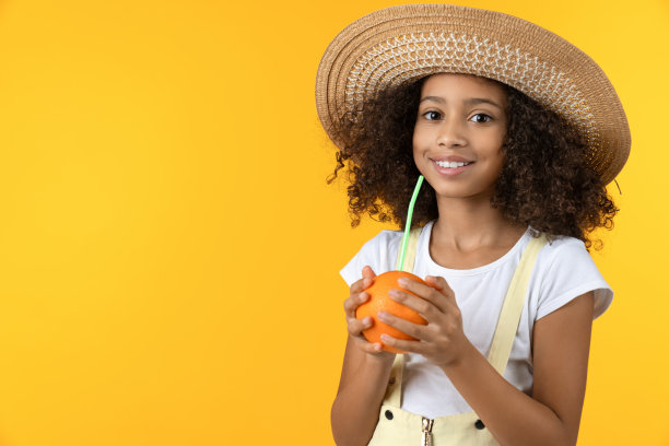 美丽的非洲女孩喝着新鲜的果汁，手里拿着一个橙子。有机食品的概念图片下载