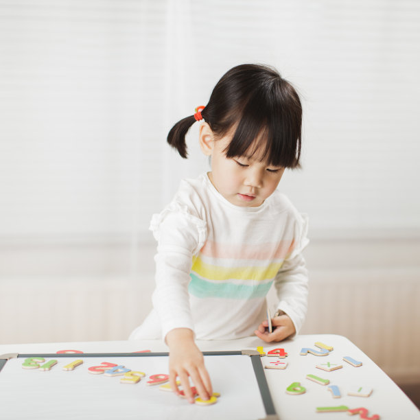 蹒跚学步的小女孩在白色背景下的白板上学习数学图片下载