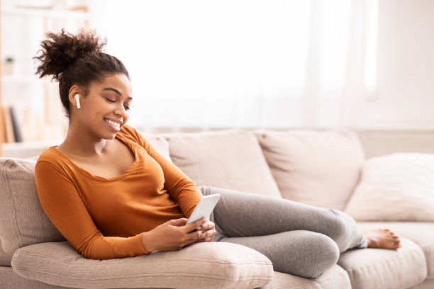 非洲裔女性坐在沙发上用智能手机听音乐图片下载