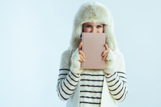 在冬天淡蓝色的背景下，女人躲在书后面图片下载