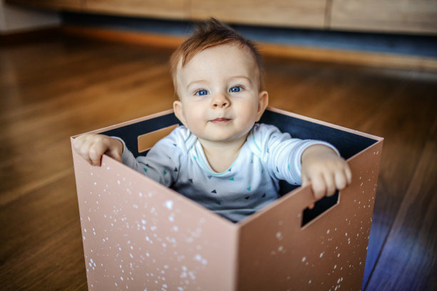 好奇可爱的金发白种人幼童和美丽的蓝色眼睛坐在盒子里看着相机。图片下载