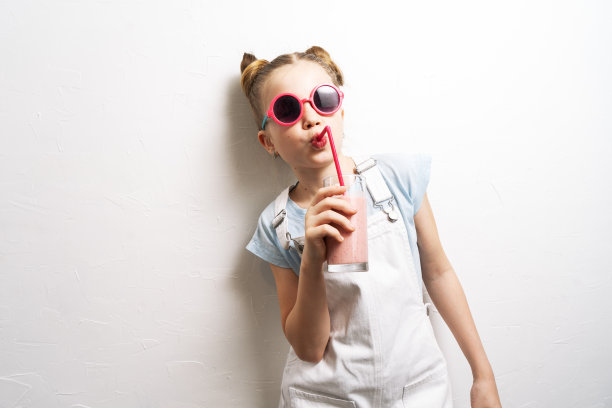 一个戴着粉色太阳镜的女孩用粉色吸管喝鸡尾酒。图片下载