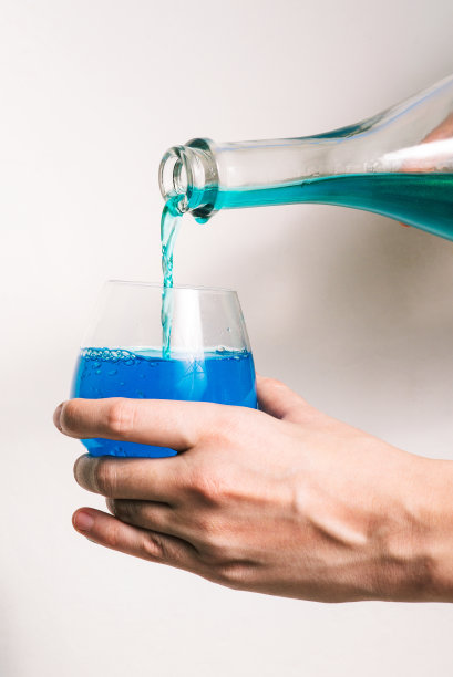 蓝色液体从玻璃瓶流入酒杯。含酒精的碳酸饮料。蓝色的香槟。图片下载