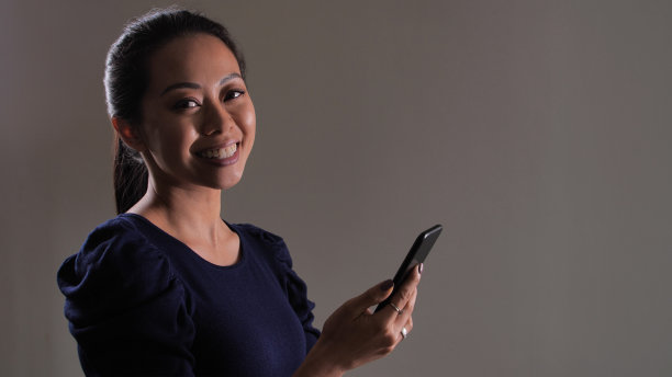 年轻女子拿着智能手机对着相机微笑。影棚拍摄。图片下载