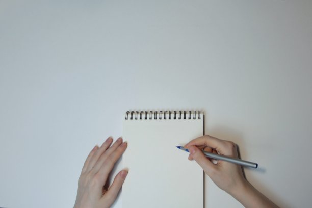 手上拿着一支圆珠笔和一个空白笔记本放在一张白色的桌子上图片下载