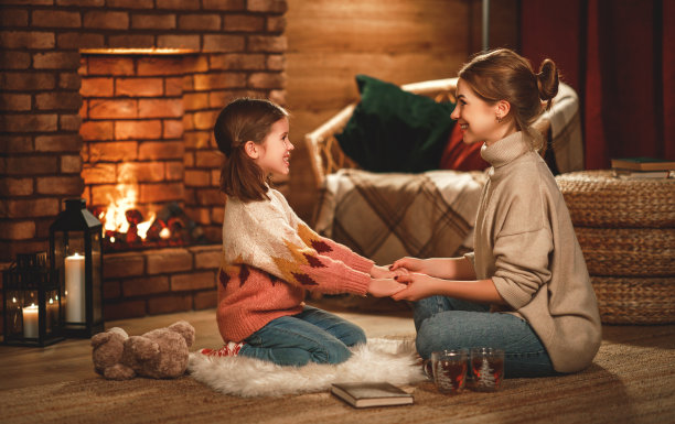 家里的母亲和孩子在冬天的晚上在壁炉边看书喝茶图片下载