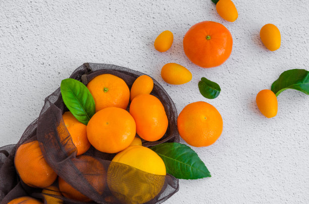 一种新鲜的有机柑橘混合在一个纺织袋在一个轻石背景。水平方向。健康食品零浪费理念，环保理念。前视图。近距离图片下载