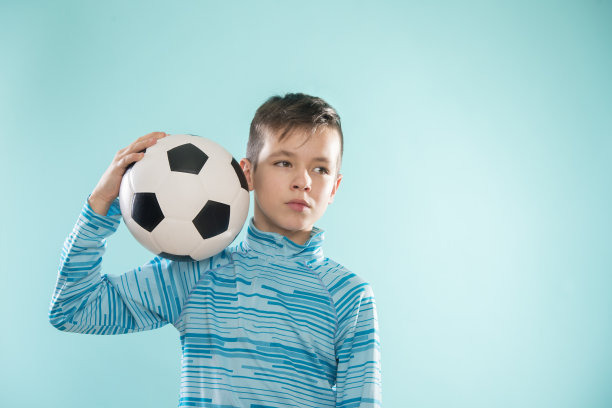 男孩与足球在蓝色的工作室背景。图片下载