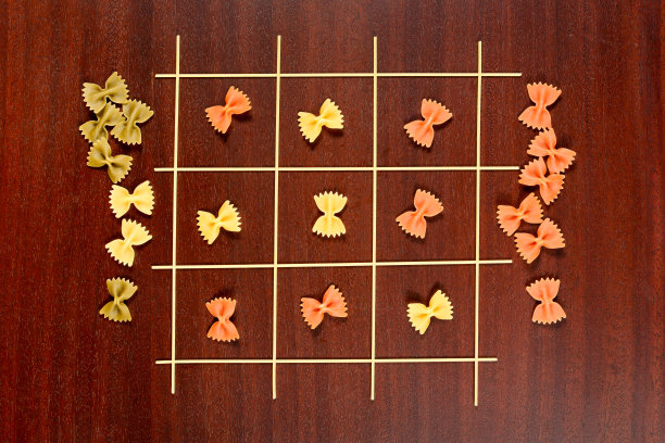 意大利面食。Tac - Toe或x和o游戏由生意大利面和不同的颜色。在棕色的木桌上放干的通心粉或意式细面条。图片下载