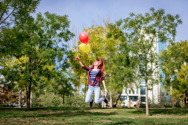 带着气球在公园里蹦蹦跳跳的快乐女人。图片下载