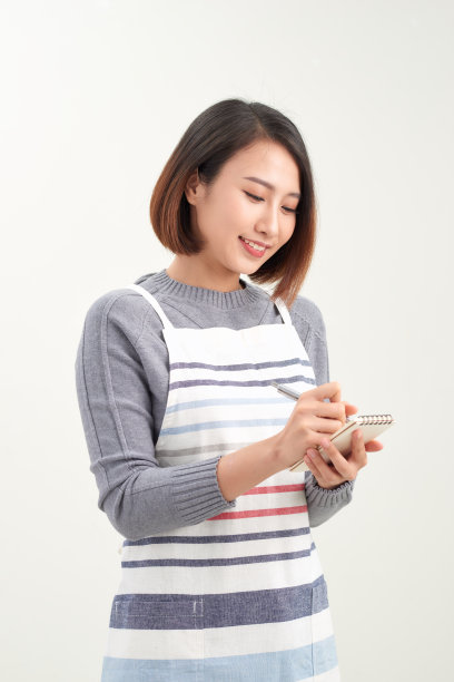 头的照片微笑的女服务员穿着黑色围裙准备接受客户订单，有吸引力的女人与笔记本和笔在手里看着相机图片下载