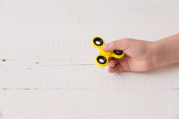 孩子的手旋转指尖陀螺装置。前视图。玩一个黄色的手旋转坐立不安玩具图片下载