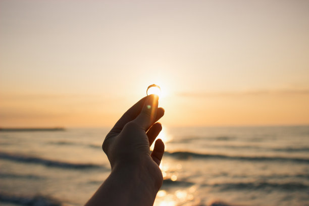 女人手里拿着订婚戒指在海面上的时间日出。在意大利海滩上求婚。胶片效果，作者对照片的处理图片下载