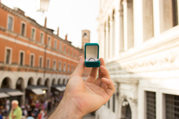 男人拿着一个带订婚戒指的蓝色盒子在威尼斯运河前。在意大利威尼斯求婚。胶片效果，作者对照片的处理图片下载