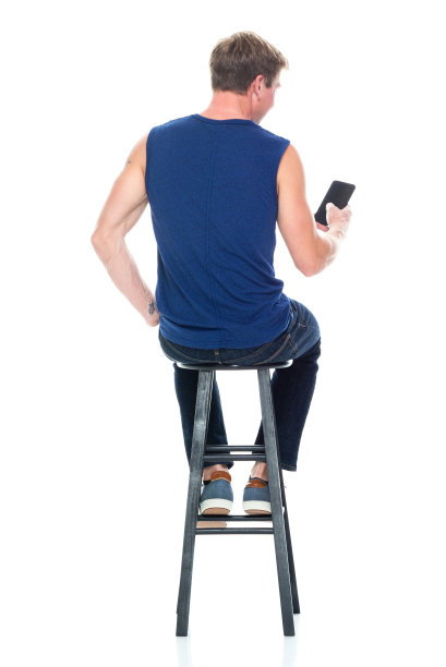 白人年轻男性无袖休息，穿着帆布鞋，使用手机图片下载