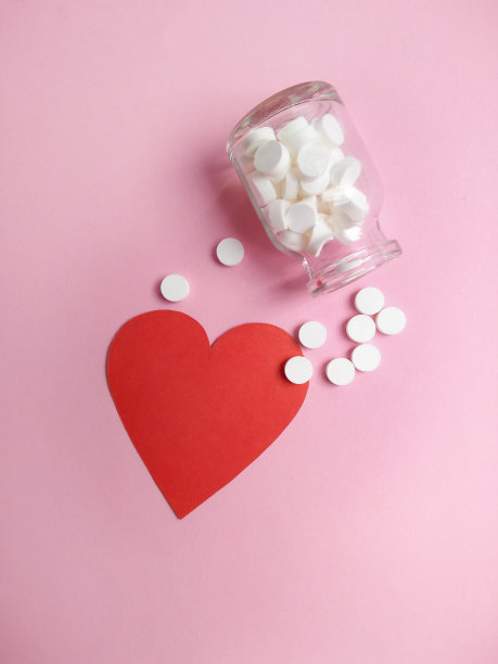 药丸从瓶子里溢出来，在粉红色的背景上呈红色的心形。图片下载