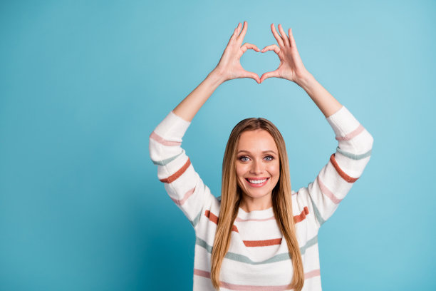 开朗积极的漂亮漂亮的女人的照片显示心形标志，微笑，牙齿灿烂，孤立的柔和的颜色背景图片下载