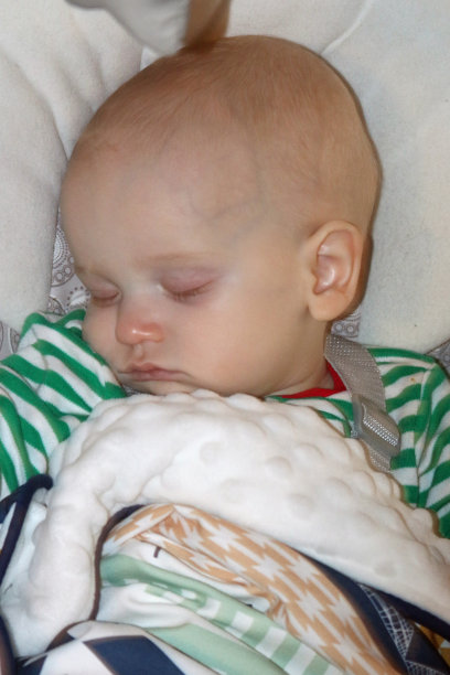 婴儿睡在绿色和白色的节日睡衣和依偎着毯子图片下载