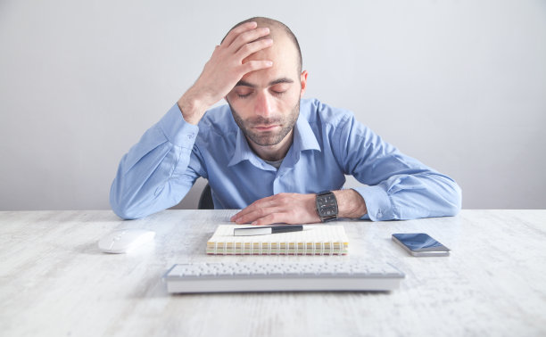 紧张的白人商人坐在办公室里碰着头。图片下载