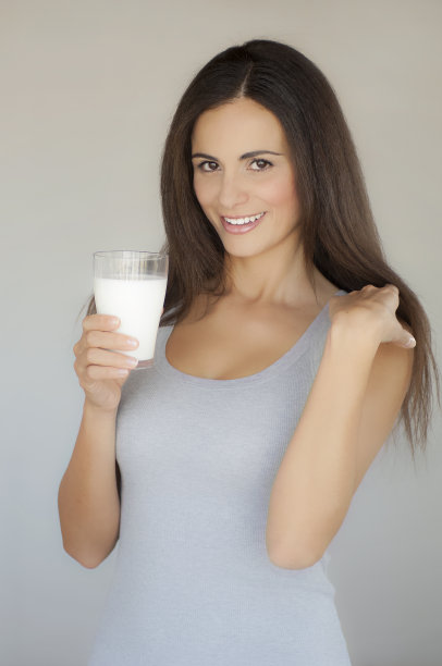半身像年轻美丽微笑的女人与长头发和一杯牛奶在她的手图片下载