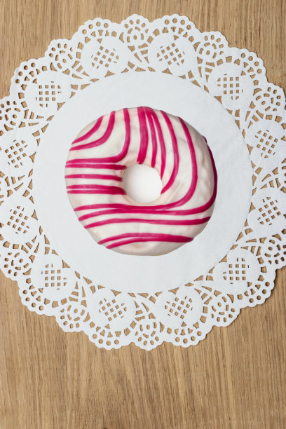 粉色甜甜甜圈躺在有花边的圆形餐巾上。图片下载