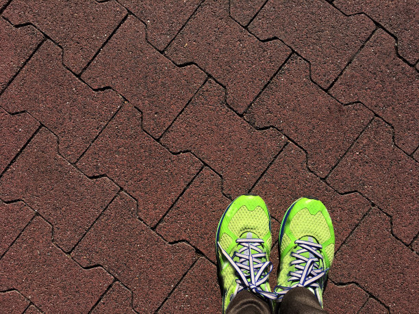 绿色跑鞋在红色混凝土砖栈道俯视图，运动概念图片下载