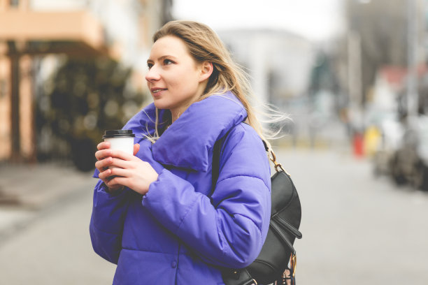 时尚美女的肖像穿着紫色的夹克在街上。概念照片与一杯热饮图片下载