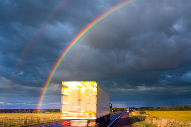 夏天晚上阵雨之后。一道明亮的彩虹耸立在公路上。卡车和客车在潮湿的柏油路上行驶。真实的照片蒙太奇或图形软件没有使用。图片下载