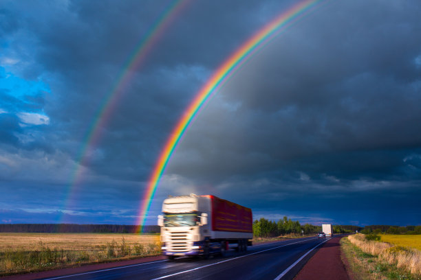 夏天晚上阵雨之后。一道明亮的彩虹耸立在公路上。卡车和客车在潮湿的柏油路上行驶。真实的照片蒙太奇或图形软件没有使用。图片下载