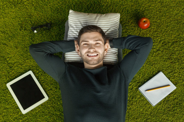 躺在绿草地毯上的家伙在平板电脑，笔记本电脑，俯视图图片下载