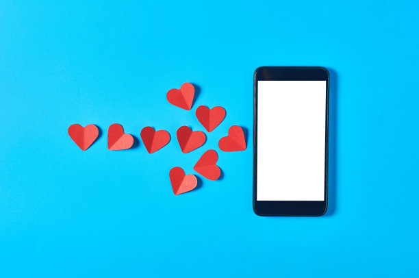 黑色智能手机与孤立的白色屏幕的文字，图片，照片和其他图形附近的箭头由红纸心形在蓝色的桌子。情人节和爱情概念。空间的文本。俯视图图片下载