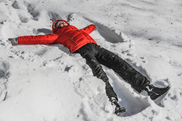一个穿着红色夹克和黑色裤子的女人在一个冬天的公园里白雪覆盖。一个女人像天使一样躺在雪中图片下载