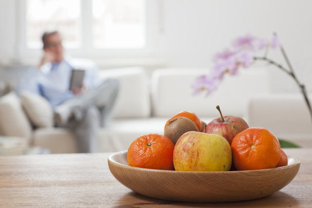 一个拿着智能手机坐在沙发上的成熟男人，前景是水果和兰花图片下载