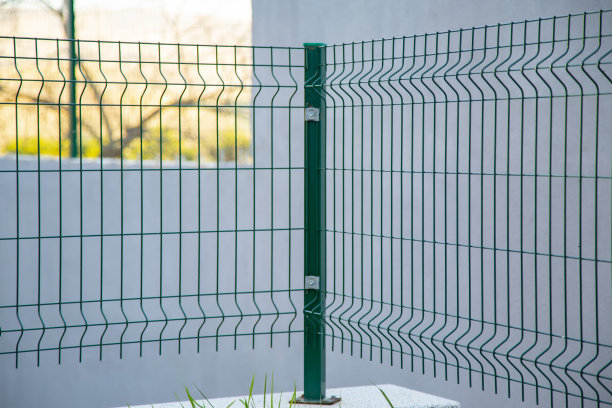 足球场的钢格栅围栏，金属围栏以散景为背景。盘绕的剃须刀线和锋利的钢倒钩在铁丝网围栏的顶部，确保安全和安全。篮球领域图片下载
