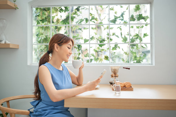 美丽的亚洲女人喝着咖啡，在窗户后面打电话图片下载