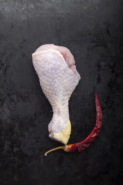 黑色背景上的生鸡腿。旁边是辣椒。图片下载