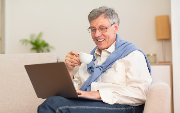 退休绅士在用笔记本电脑，坐在沙发上喝咖啡图片下载