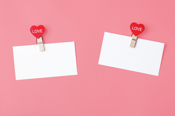 白色纸条与心衣夹与文字爱，在粉红色的背景。情人节的概念，爱的宣言。本空间图片下载