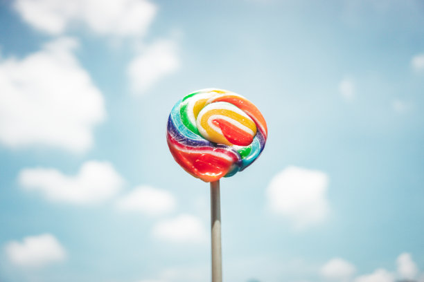 五颜六色的彩虹和棒棒糖在蓝天白云的背景下旋转图片下载