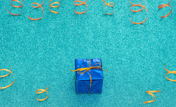 包装经典的蓝色礼盒与金色丝带在庆祝蓝色背景与明亮的派对飘带。生日，派对，乐趣，快乐的概念。问候、邀请卡。平铺，俯视图，拷贝空间。图片下载