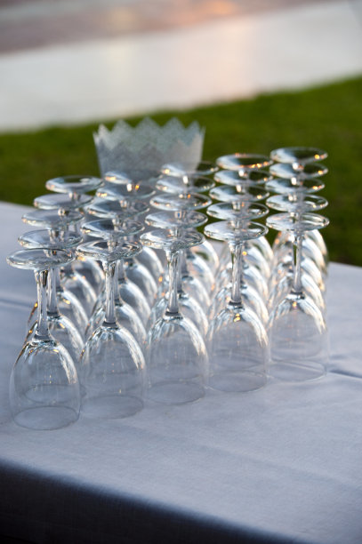 25只透明玻璃杯，白色台布，绿色背景，夕阳的余晖反射在玻璃杯和背景上图片下载