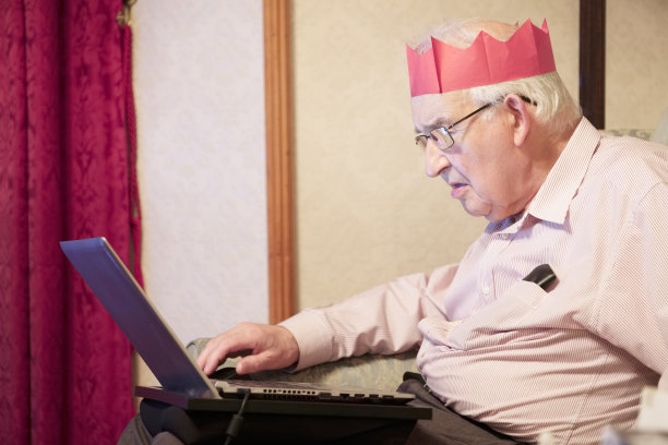 派对上戴着红纸帽子的老人一边庆祝一边玩电脑笔记本图片下载