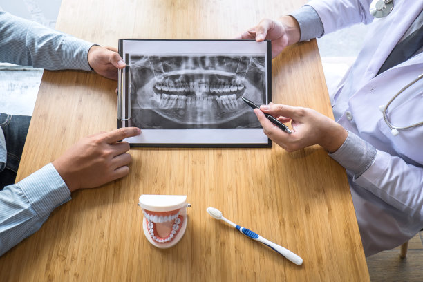 专业牙医与病人讨论颌骨和牙齿的x光照片，解释会诊治疗的问题，并在笔记本上写下病人的病史图片下载