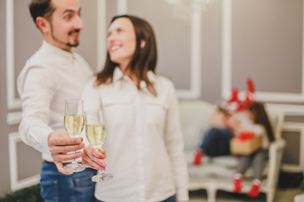 在圣诞彩灯和圣诞树下，用香槟杯敬酒。图片下载