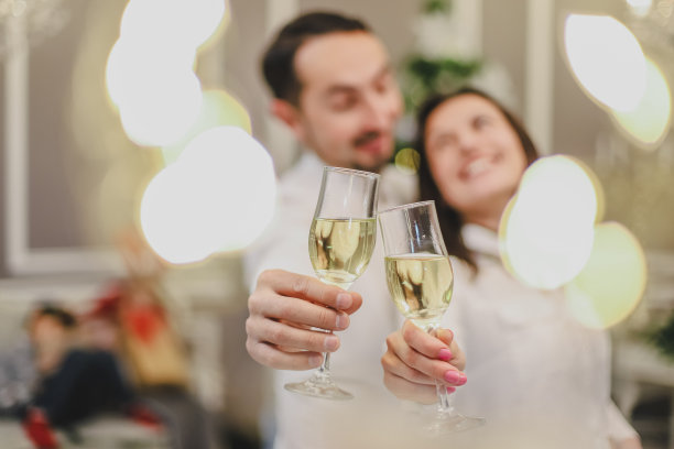 在圣诞彩灯和圣诞树下，用香槟杯敬酒。图片下载