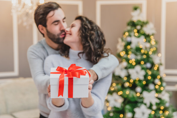散焦的男人和女人拿着一份用红丝带系着的礼物，看着镜头微笑着。图片下载