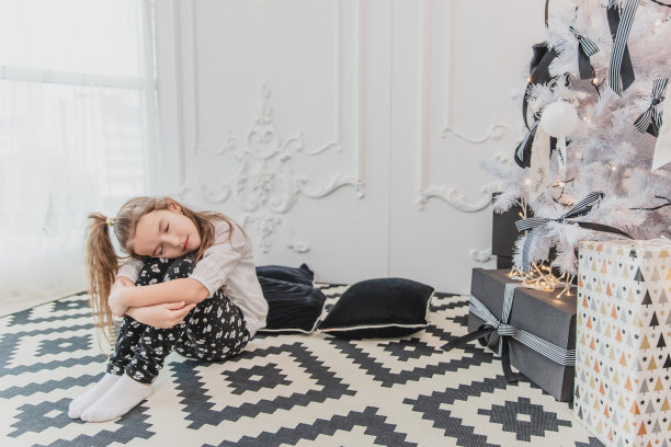 美丽的小天使女孩抱着膝盖，完美地睡在圣诞树旁。图片下载