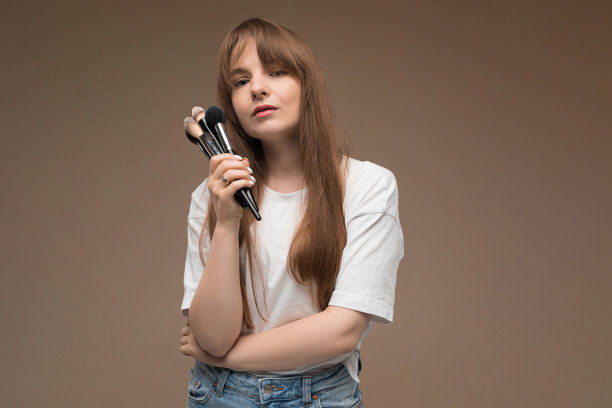 好女孩拿着化妆刷在深棕色的背景图片下载