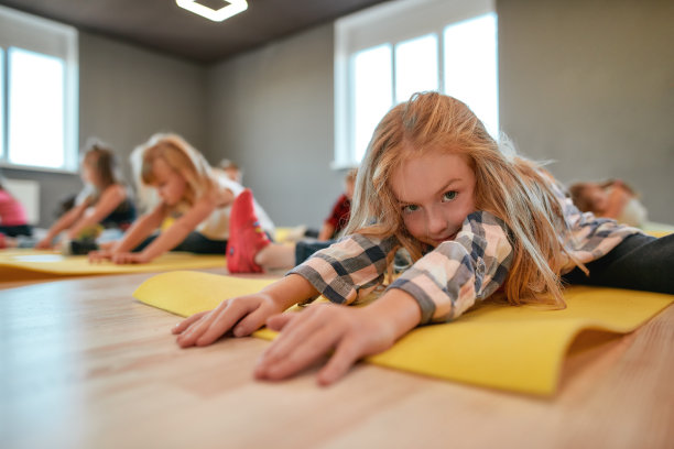 一个可爱的小女孩坐在瑜伽垫上的特写，伸展她的身体。一群孩子在舞蹈室做体操图片下载