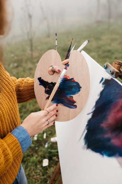 近距离的照片年轻的女艺术家工作在绘画户外。她拿着油画颜料，艺术家的画笔，帆布和调色板。她在调色板上调色。手关闭。图片下载